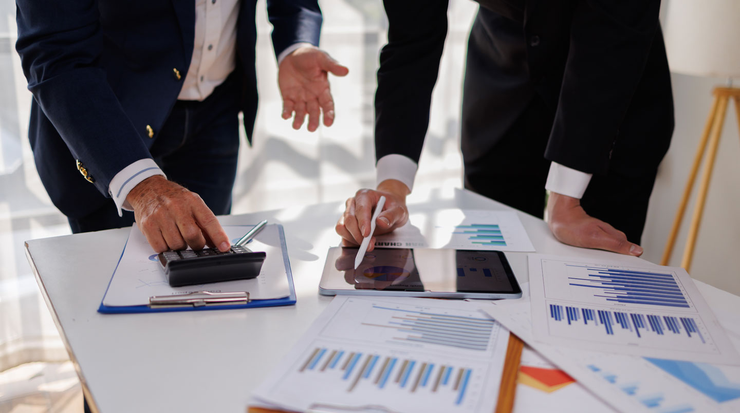 Mains consultant un rapport financier imprimé ouvert sur un bureau professionnel, avec ordinateur portable et documents administratifs en arrière-plan